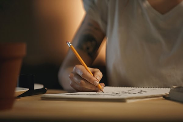 Cropped photo of young woman designer sitting indoors at night writing notes.